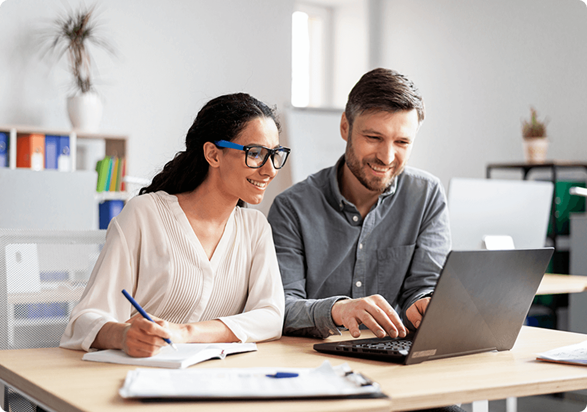 A man and woman sitting at a table looking at a laptop.